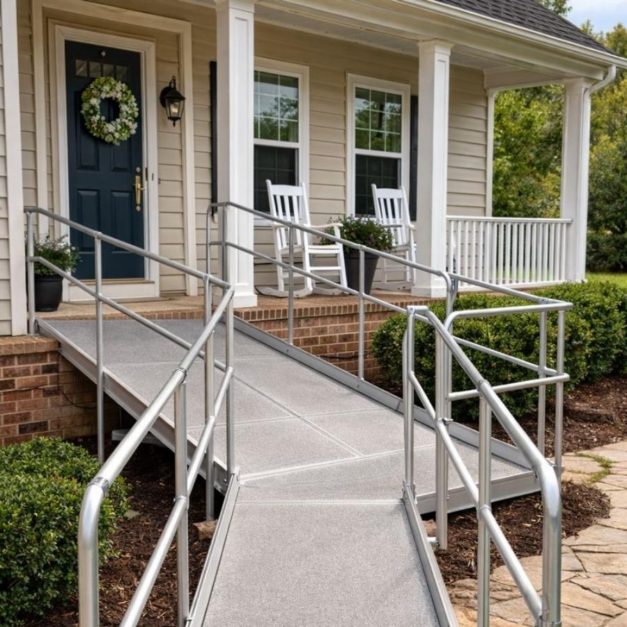 A modular silver aluminum wheelchair ramp with double handrails leading to the front porch of a tan residential home.